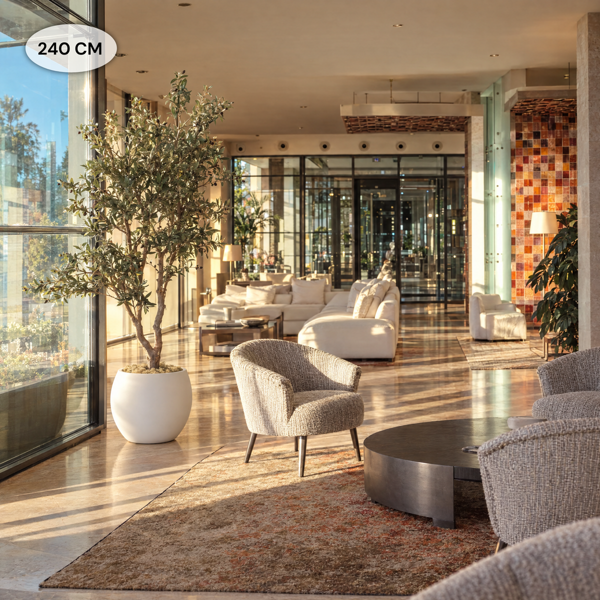 Kunst olijfboom van 240 cm in witte pot bij de glazen gevel van een luxe hotellobby