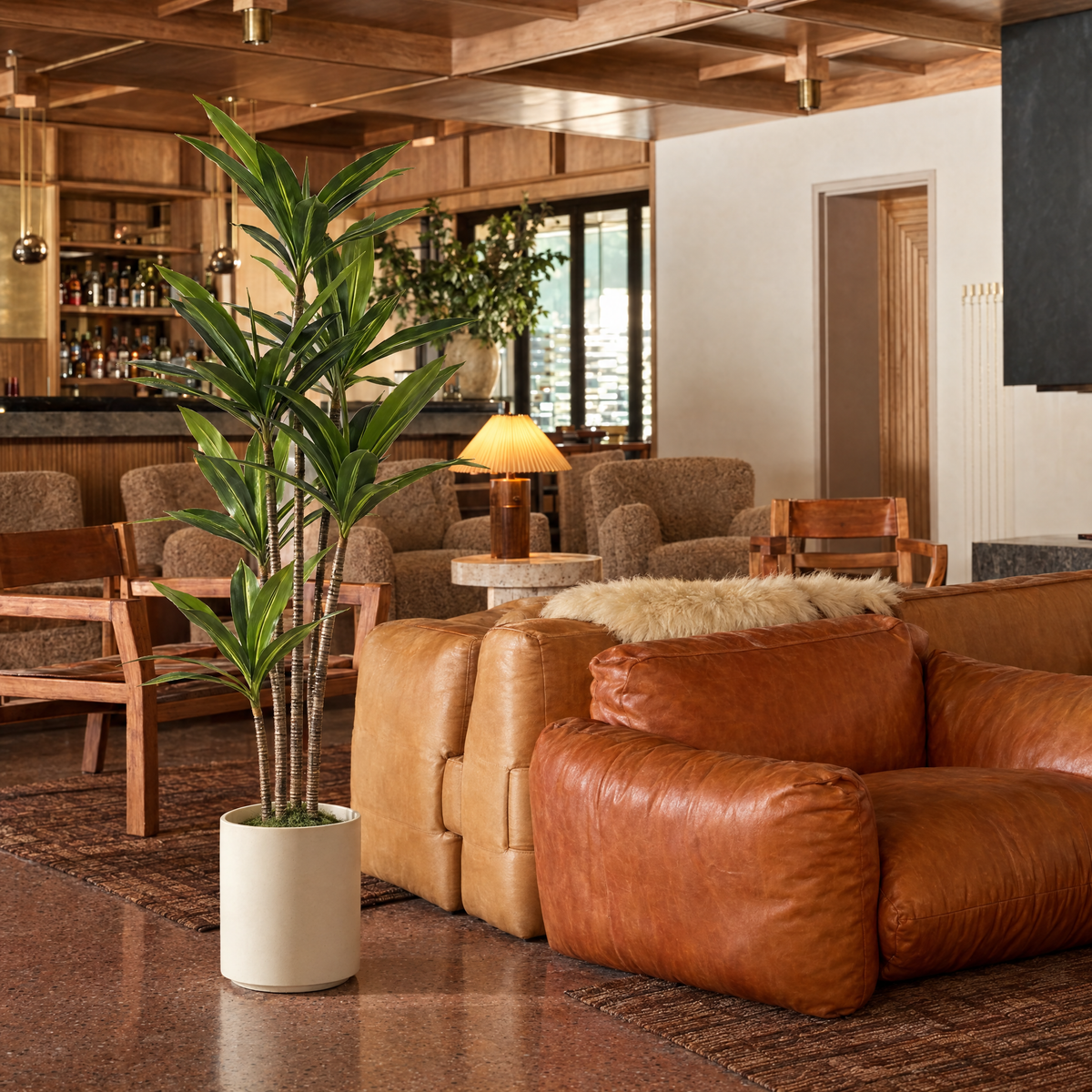 Kunst dracaena van 180 cm in crèmekleurige pot naast een leren bank in een warme hotellounge met bar